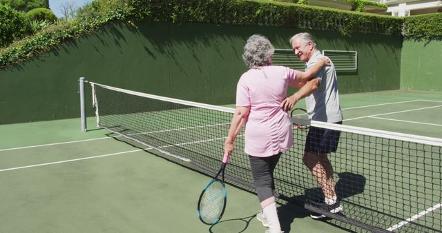 Happy caucasian senior couple embracing over the net at outdoor tennis court after playing a game. active retirement lifestyle sports hobby.