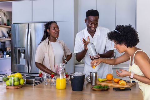 African american friends preparing fresh citrus cocktails at modern kitchen island