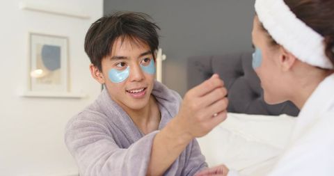 Couple applying hydrogel under-eye patches in cozy bedroom spa self-care moment