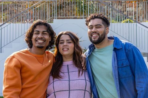 Three friends smiling and embracing on outdoor steps, casual urban lifestyle portrait