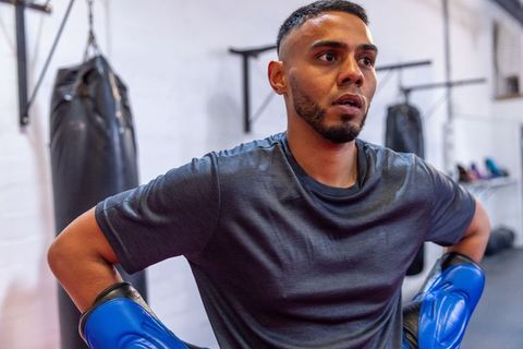 Focused boxer training with blue gloves in urban gym after intense sparring round