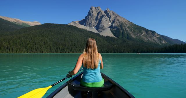 This image depicts a woman kayaking on a clear, calm lake with a magnificent mountain in the background. Perfect for promoting outdoor recreation, travel destinations, nature conservation, adventure activities, and eco-friendly tourism.