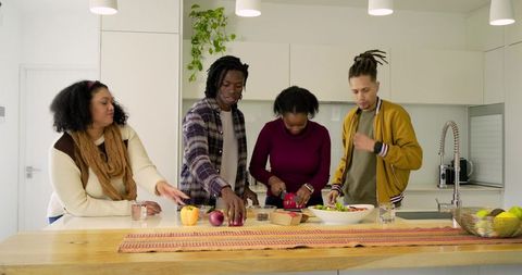 Diverse friends chopping fresh vegetables together at modern kitchen island preparing healthy salad