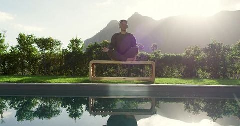 Woman meditating outdoors by reflecting pool with mountain view