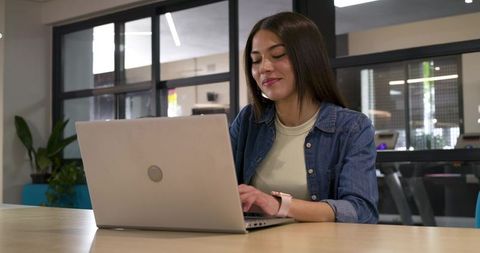 African woman working on laptop in modern coworking space with denim jacket and smartwatch