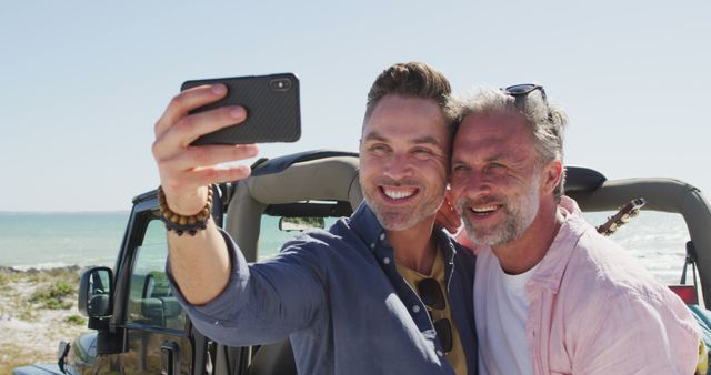 Happy caucasian gay male couple taking selfies and smiling by car on sunny day at the beach. summer road trip and holiday in nature.