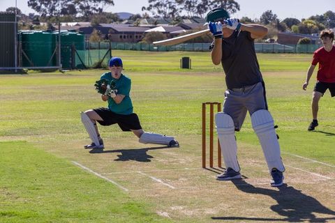 Youth cricket players batting and wicketkeeping in suburban park on sunny day