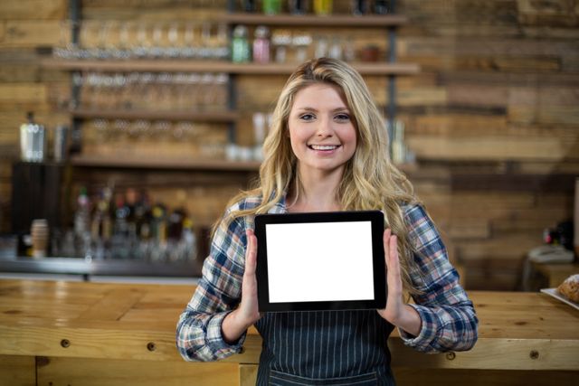 Portrait of smiling waitress standing at counter and showing digital tablet in cafe