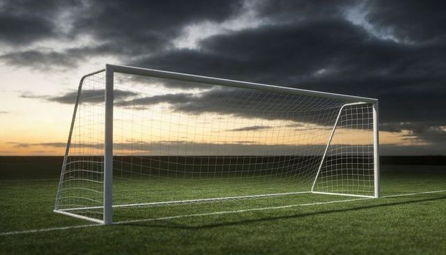 Empty white soccer goal standing at dusk on green pitch with dramatic cloudy sky