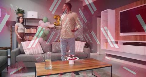 Couple celebrating at home with man holding dessert plate and gold 3 balloon pastel decor