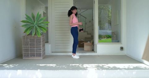 Young woman standing on modern front porch holding smartphone during move