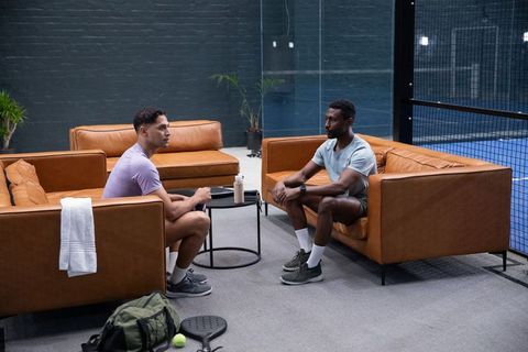 Two teammates discussing strategy in sports lounge by indoor paddle court