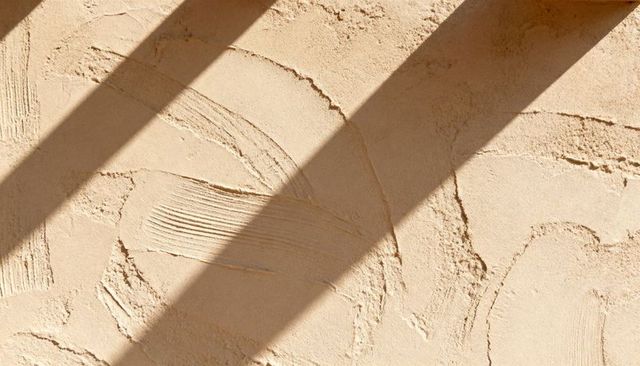Beige textured plaster wall with trowel marks, combed grooves and diagonal sunlight bands