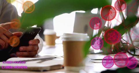 Tapping smartphone at coworking table with coffee and laptop during cyber monday
