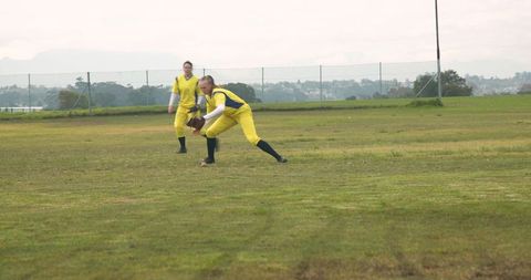 Female softball players in yellow uniforms fielding ground ball