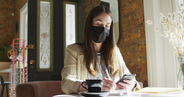 Woman Wearing Face Mask Working on Phone and Notebook in Cafe - Download Free Stock Images Pikwizard.com