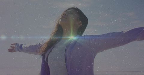 Woman embracing ocean breeze with outstretched arms and sun flare