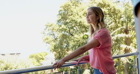 Woman Leaning Against Balcony Railing Enjoying Sunny Day Outdoors