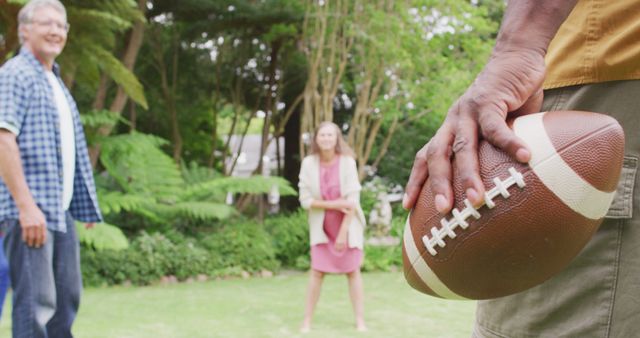Image of happy diverse female and male senior friends playing american football in garden. retirement lifestyle, spending quality time with friends.
