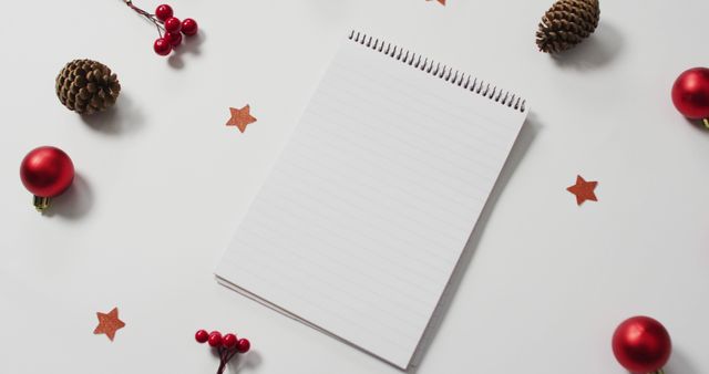 Image of red christmas decorations with notebook on white background. christmas, tradition and celebration concept.