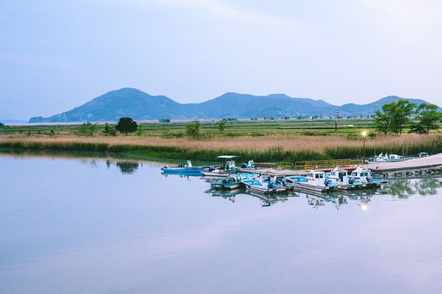Calm scene of boats docked at lakeside with a view of distant mountains at twilight. Peaceful reflective waters create a serene atmosphere, perfect for conveying tranquility and nature's beauty. Ideal for travel brochures, landscape photography, and outdoor adventure promotions.