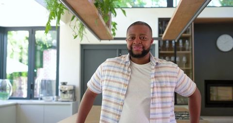 Confident man standing at kitchen island wearing casual striped shirt, bright interior