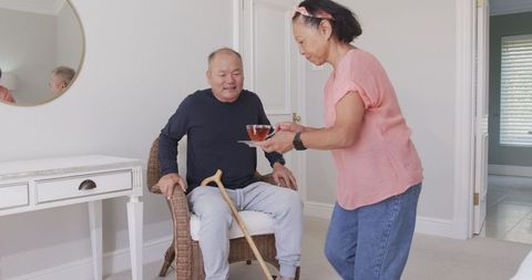 Senior caregiver helping elderly man sit at home with comfort