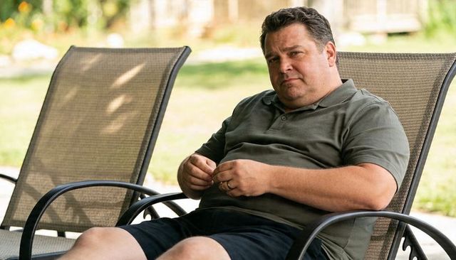 Middle-aged man relaxing on mesh patio chair in sunny backyard wearing polo and shorts