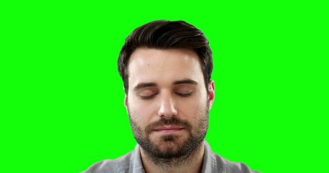 This image shows a man with eyes closed, meditating in front of a green screen background. It can be used for concepts related to calmness, mindfulness, relaxation, and mental health wellness. The green screen allows for easy background replacement in various multimedia and creative projects.