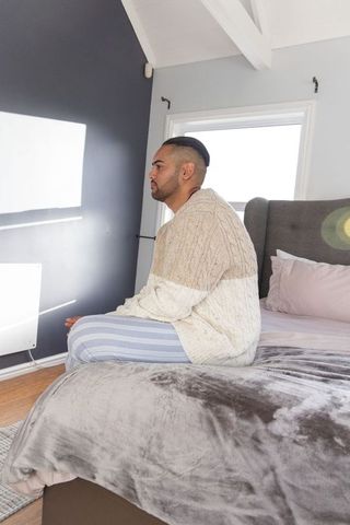 Mid-adult man sitting on bed edge in loft bedroom wearing cable knit sweater