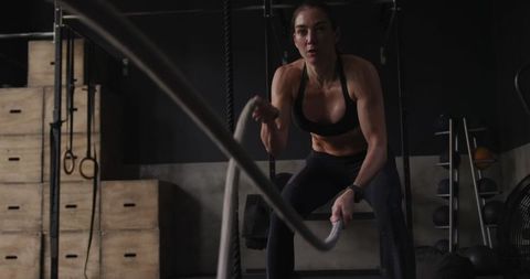 Fit woman engaging in battle ropes exercise in gym