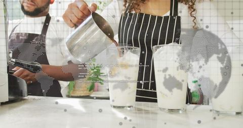 Barista pouring iced espresso into glasses at counter, striped apron, coffee teamwork