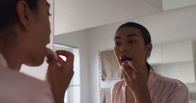 This image shows a woman applying lipstick in front of a bathroom mirror. The scene reflects typical morning self-care routines, emphasizing beauty and personal grooming. This image can be used in articles or websites related to beauty tips, makeup tutorials, personal care routines, and lifestyle blogs.