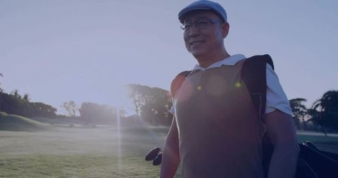 Senior golfer walking fairway carrying golf bag at sunrise with lens flare and mist