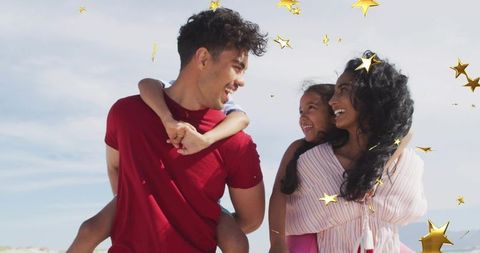 Playful family enjoying piggyback smiles on sunny beach with floating gold stars