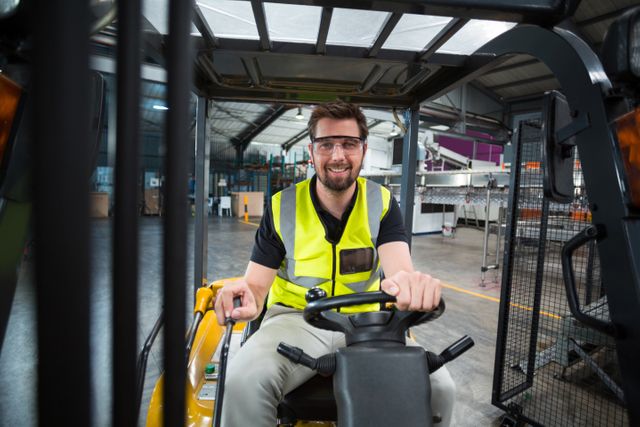 Portrait of smiling factory worker driving forklift in factory