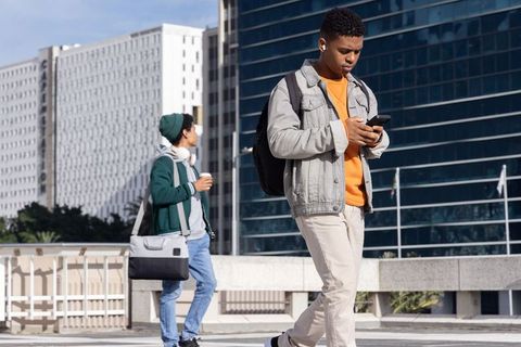Urban young men walking with smartphone and headphones commuting across city bridge