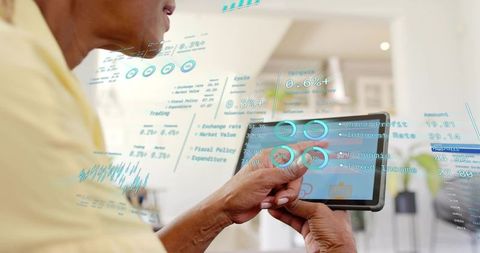 Senior woman holding tablet tapping augmented reality financial dashboard at home
