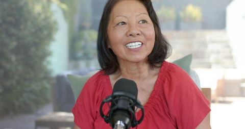 Mature woman recording podcast on patio with professional microphone and natural light