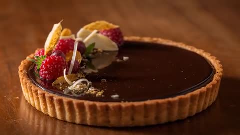 Camera moving closer centering on wooden tabletop showing glossy chocolate tart with raspberries