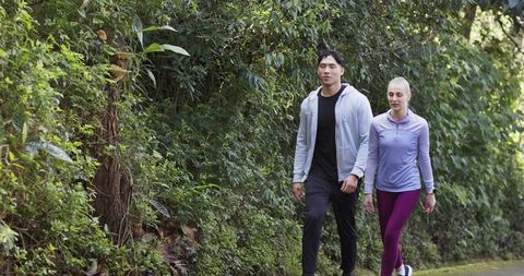 Diverse couple walking on mossy park trail in athletic wear enjoying outdoor fitness and nature