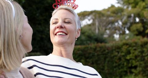 Mature woman laughing and wearing merry christmas headband celebrating with friend outdoor