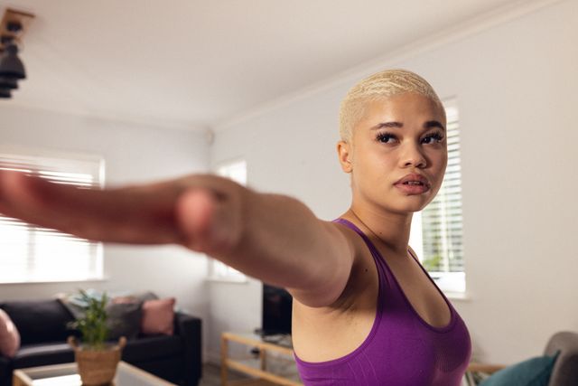 Biracial young woman with short hair stretching arm during home workout. Ideal for content related to fitness, yoga, healthy living, home exercise routines, and wellness. Can be used in blogs, social media posts, fitness apps, and lifestyle magazines.