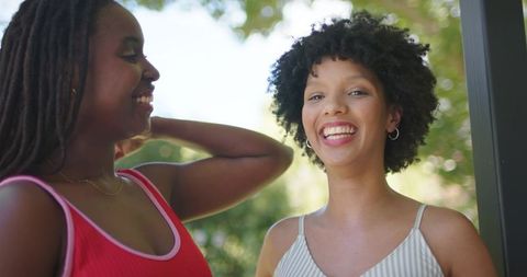 Two african american women laughing and chatting on sunlit porch near doorway