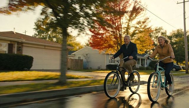 Senior couple cycling cruiser bikes through autumn suburb at golden hour, wet road