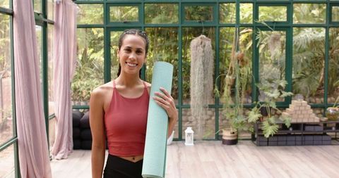 Smiling Woman Holding Yoga Mat in Glasshouse for Wellness Retreat