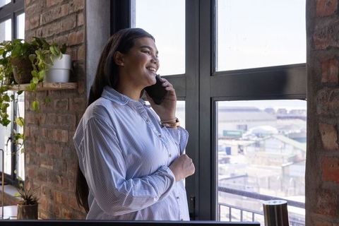 Pregnant Woman in Loft Office Smiling While on Call by Window