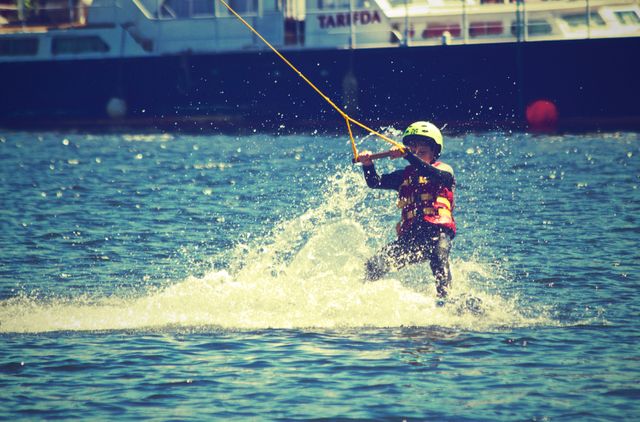 Person wakeboarding wearing helmet and life jacket. Suitable for scenes depicting outdoor water sports, recreational activities, summer fun, and active lifestyles.