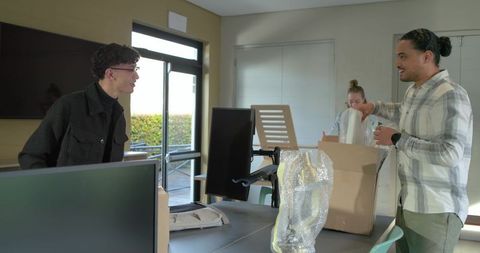 Coworkers unpacking office equipment at modern conference table during collaborative setup