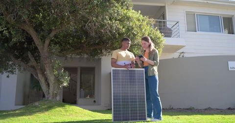 Couple examining smartphone planning residential solar panel installation on front lawn
